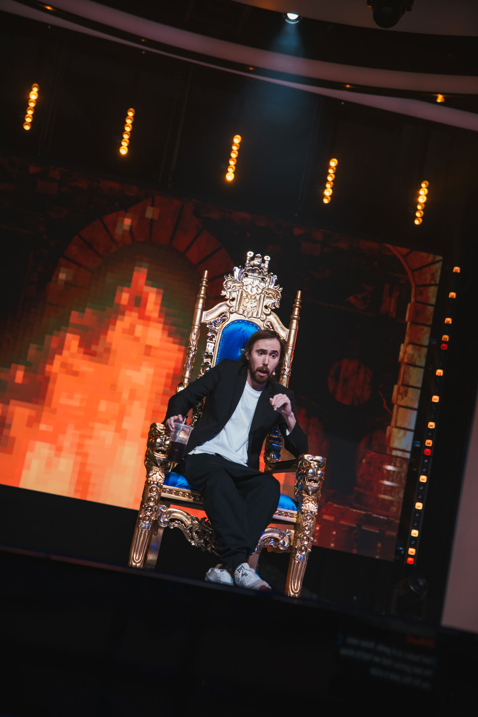 Asmongold sitting on a throne on stage.